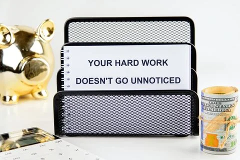 A motivating note about hard work sits on a desk alongside a golden piggy ban Stock Photos