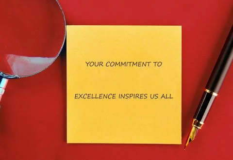 A motivational note emphasizes commitment to excellence placed on a red desk. Stock Photos