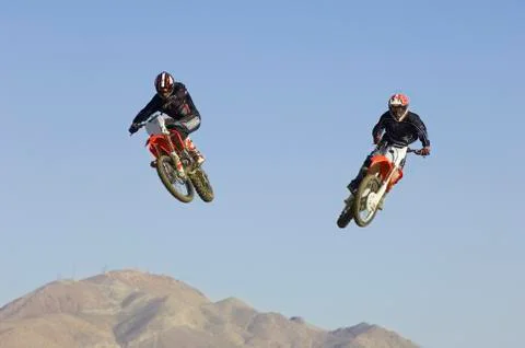 Motocross Racers Performing Stunt In Midair Against Blue Sky Stock Photos
