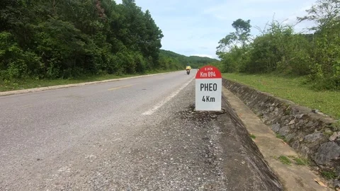 A motorbike passes by a road post on an empty green road in Vietnam Stock Footage 219224148