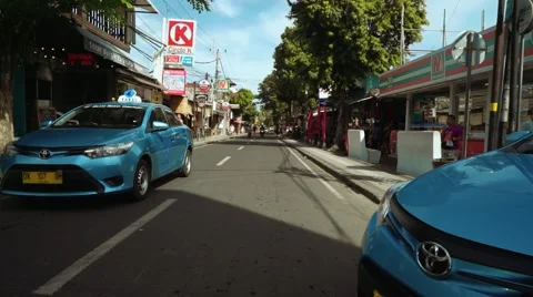 Motorbiker rides between two blue bird taxi cars, Legian street Stock-Footage 65300487