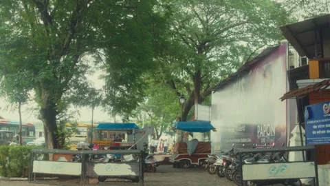 Motorbikes and Rickshaws Parked Under Trees Along Riverside Urban Street Stock Footage 341757020
