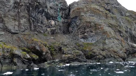 Motorboat passing by rugged rocky cliffs of Antarctic Peninsula coast Antarctica Stock Footage 335288036