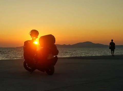 A motorcycle in the rays of the setting sun stands on the seashore. Stock Photos