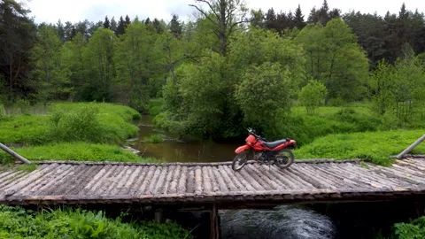 Motorcycle is standing on a bridge over a tiny clear river in the wild Stock Footage 169924529