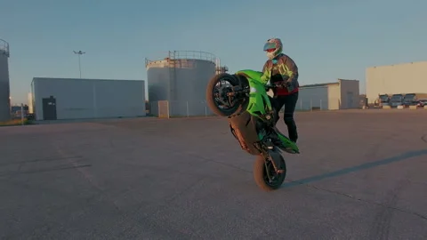 Motorcyclist practice circle tricks on the rear wheel outdoor in sun beams Stock Footage 105049103