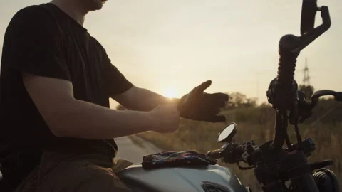 A motorcyclist puts on his gloves at sunset Stock Footage 253446597