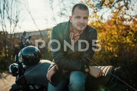 Motorcyclist sits on an old cafe-racer motorcycle, autumn background Stock Photos