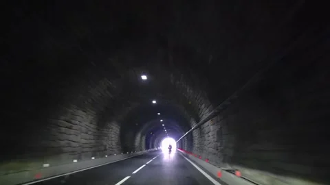 Motorcyclists driving through dark stone highway tunnel toward bright exit POV Vídeo Stock 346250238