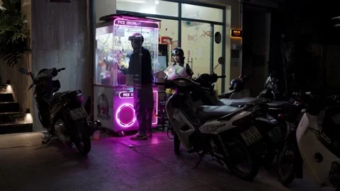 Motorcyclists take a break to play a neon-lit claw crane game in Ho Chi Minh Stock Footage 332989577