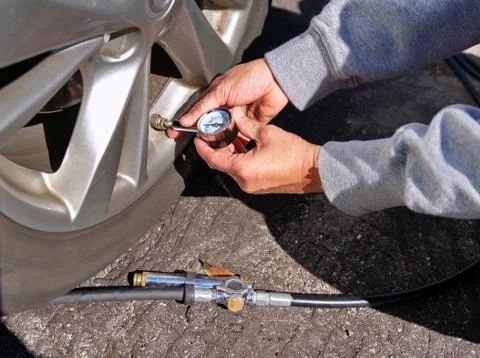 Motorist hands checking and servicing tire pressure at a local gas station. Stock Photos