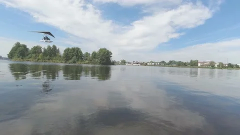 Motorized hang glider flies over lake and green trees Video stock 147171706