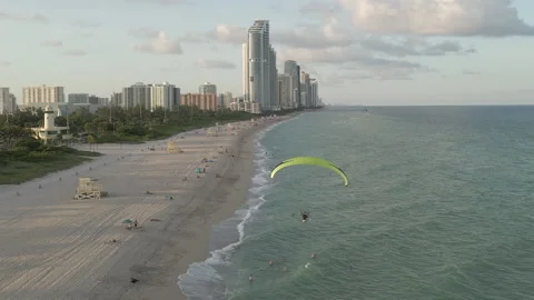 Motorized paraglider flies low over sandy Miami Beach in afternoon sun 動画素材 167985829