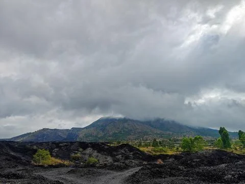 Mount Batur Volcano and Black Lava Field Under Dramatic Overcast Sky Фото