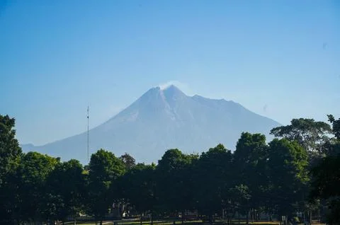Mount Merapi rises beyond a green treeline near Prambanan Temple beneath a .. 스톡 사진