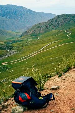 Mountain backpack on cliff edge, overlooking scenic valley road. Kyrgyzstan Stock Photos