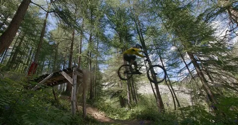 A mountain biker jumps froma big jump in a forest. Stock Footage