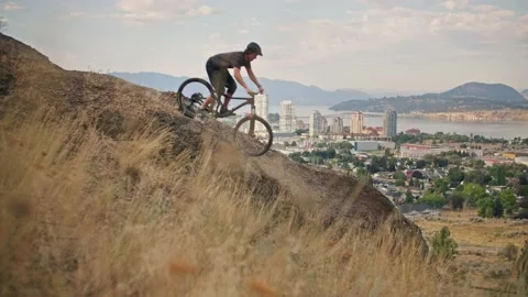 Mountain biker rides down steep mountain cliff with scenic views 库存影片 212162424