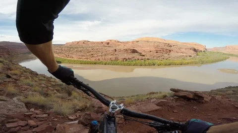 Mountain Biker Riding Down Trail Towards A River In The Desert Vídeo Stock 114335048