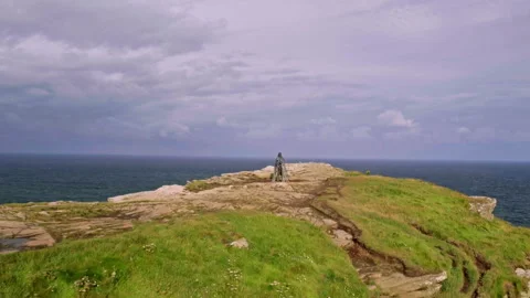 Mountain biker standing on a dramatic cliff edge overlooking the ocean Stock Footage 336369367