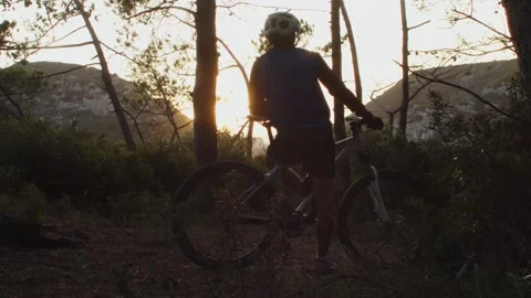 Mountain Biker watching the sunset sunshine in a forest in Slow Motion Stock Footage 260260340
