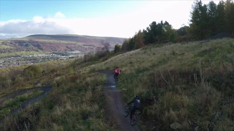 Mountain bikers cycling down trail with multiple jumps together, drone aerial 4K Stock Footage 101109211