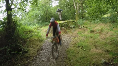 Mountain bikers cycling towards camera off of large rock drop, drone aerial 4K Video stock 101107210