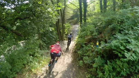 Mountain bikers flying through forest over big jump, drone aerial 4K Stock Footage 101106724