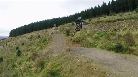 Mountain bikers go over multiple huge jumps one after another, drone aerial 4K Stock Footage 101110175