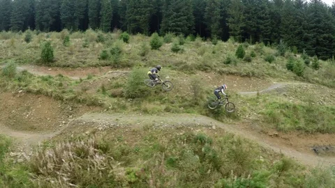 Mountain bikers going over multiple large jumps with tricks, drone aerial 4K Stock Footage 101154463