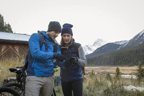 Mountain biking couple using smart phone outside mountain cabin, Rocky Mountains Stock Photos
