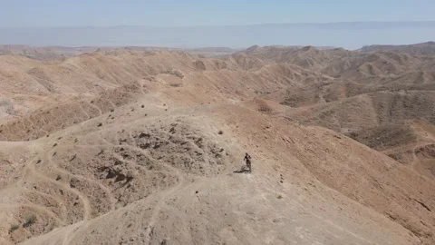 Mountain biking downhill through a desert sharp mountain ridge, aerial 스톡 동영상 239760057