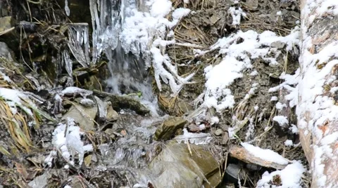 Mountain brook flows on stony snowy soil with icicles and ice Stock Footage 50493629