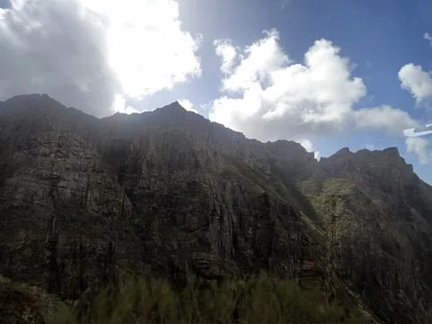 Mountain cliffs under dramatic cloudy sky with sunlight breaks Photos