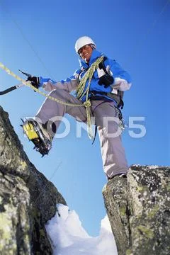 Mountain climber stepping over crevasse on mountain and smiling Stock Photos