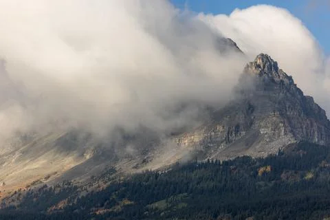 A mountain covered in clouds with a few trees in the foreground Stock Photos