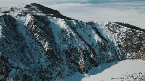 The mountain is covered with snow, the rock is surrounded by frozen Lake Baikal Stock Footage 150904538
