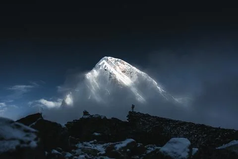 Mountain explorer on rock summit standing at night in front of snow cloudy hi Stock Photos