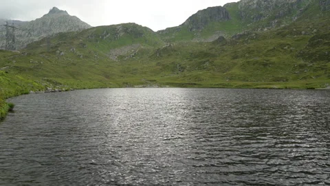 Mountain lake on a cloudy day, surrounded by mountains, green meadows with high Stock Footage 161743292
