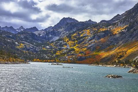 Mountain Lake with Dramatic Fall Foliage and Granite Peaks Under Cloudy Sky Foto stock