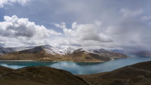 Mountain Lake Panorama with Snow-Capped Peaks and Dramatic Clouds Foto stock