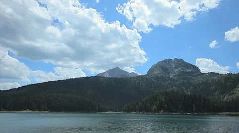 Mountain lake, slopes with pine trees,, rocky mountain, blue sky, white clouds Stock Footage 8558106