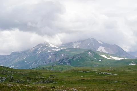 Mountain landscape with clouds and green alpine meadows in the foreground. Stock Photos