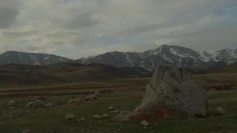 Mountain landscape with large rock in foreground and snow capped peaks Vidéo 333953195