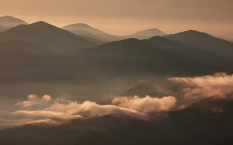 Mountain landscape with low clouds, rays of light and morning fog at dawn. Stock Photos