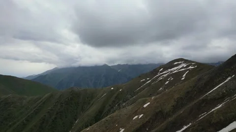 Mountain landscape with rolling hills and cloudy sky over snow-capped peaks Video stock 336963559
