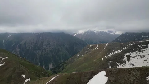Mountain landscape with rolling hills and snow-capped peaks under cloudy sky Stock Footage 336963659
