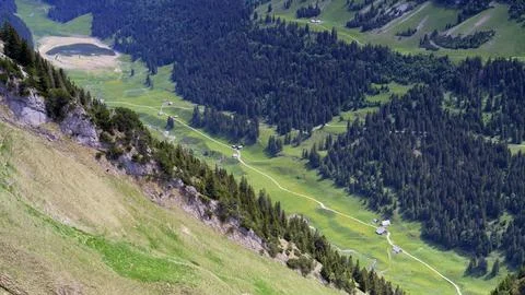 Mountain landscape with winding path and distant houses in summer on a clear Stock Photos