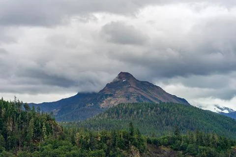 Mountain peak with overcast cloudy sky in a forest in Alaska Stock Photos