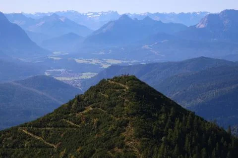Mountain peak surrounded with trees and visible zig zag path and cross in centre Stock Photos